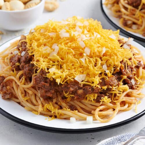 Side view of a plate of Cincinnati chili with shredded cheese and diced onions.