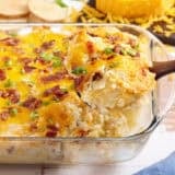 Side view of a twice baked potato casserole with a spoon taking some out the dish.
