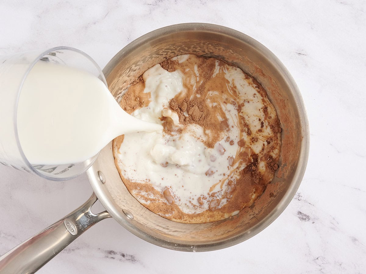 Milk being poured into a saucepan with cocoa powder.