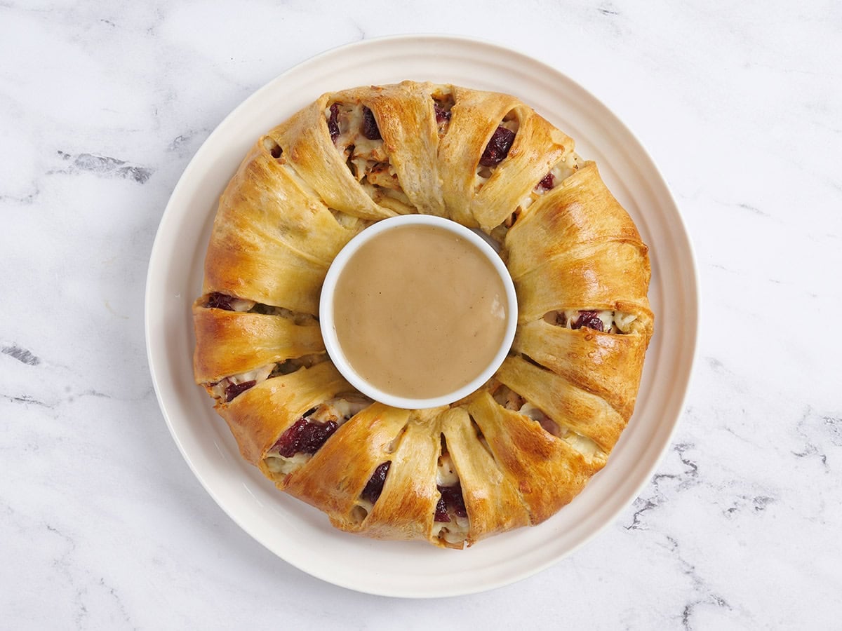 Baked holiday wreath with a bowl of gravy in the middle.