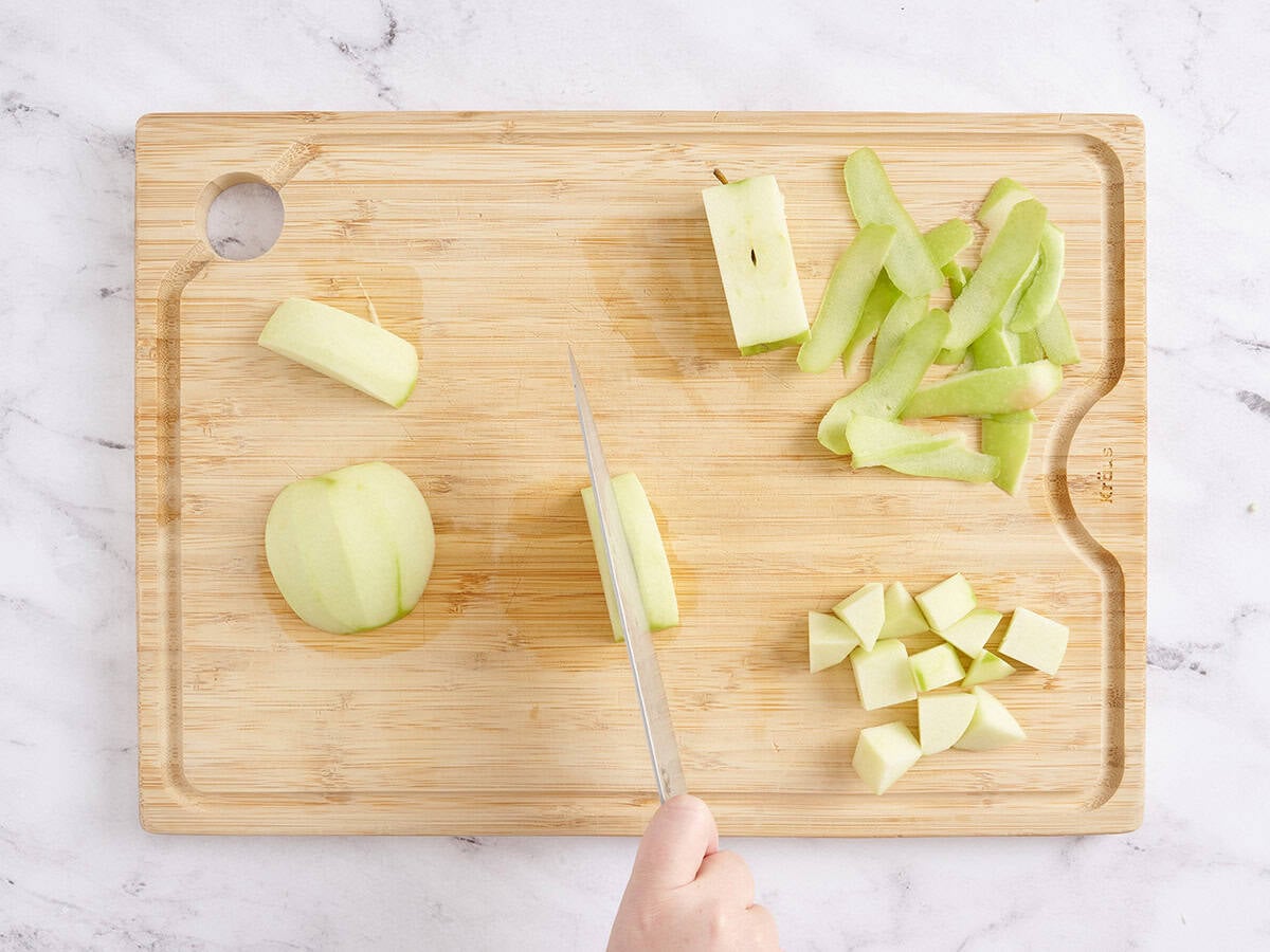 A knife dicing apples on a wooden cutting board.