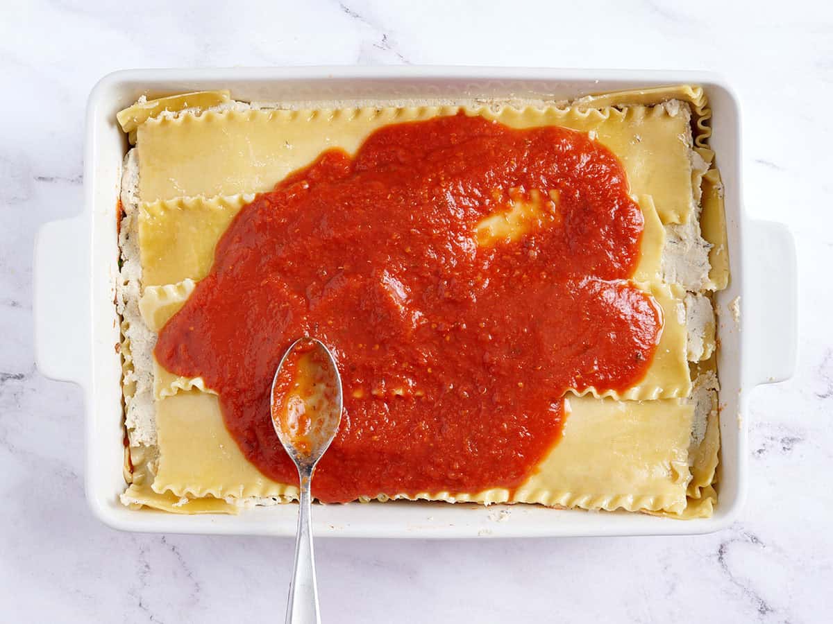 Marinara sauce added to vegan lasagne.