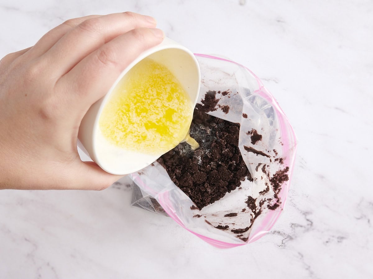 Butter being poured into a ziplock bag of cookie crumbs.