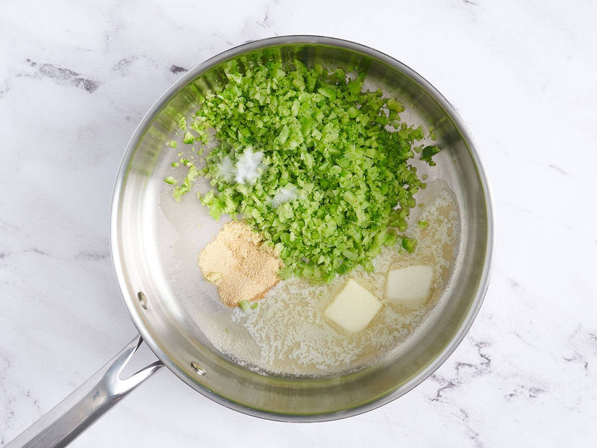 Diced broccoli in a saucepan with seasonings and butter.