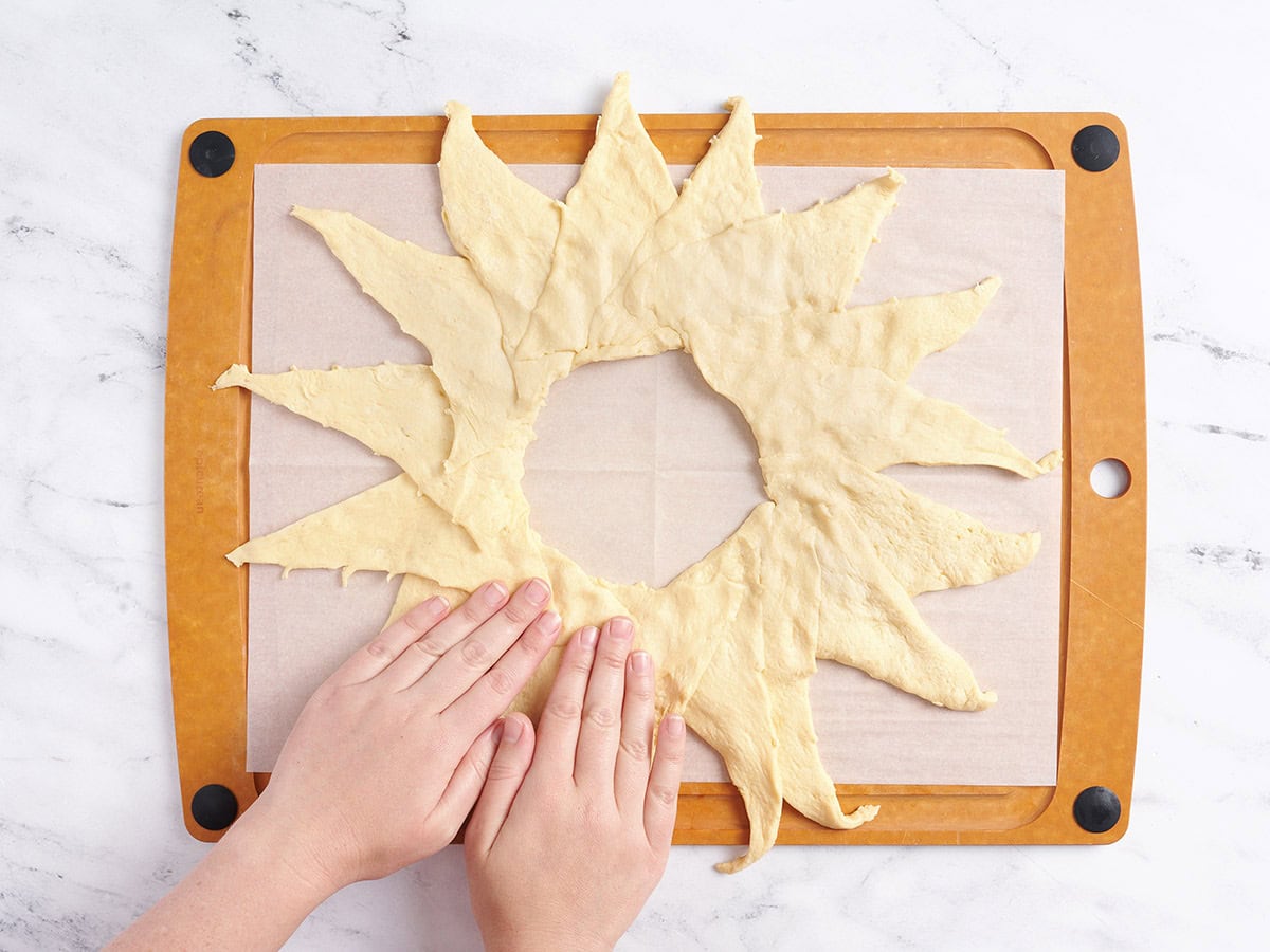 Pressing down on the crescent rolls so they stick together.