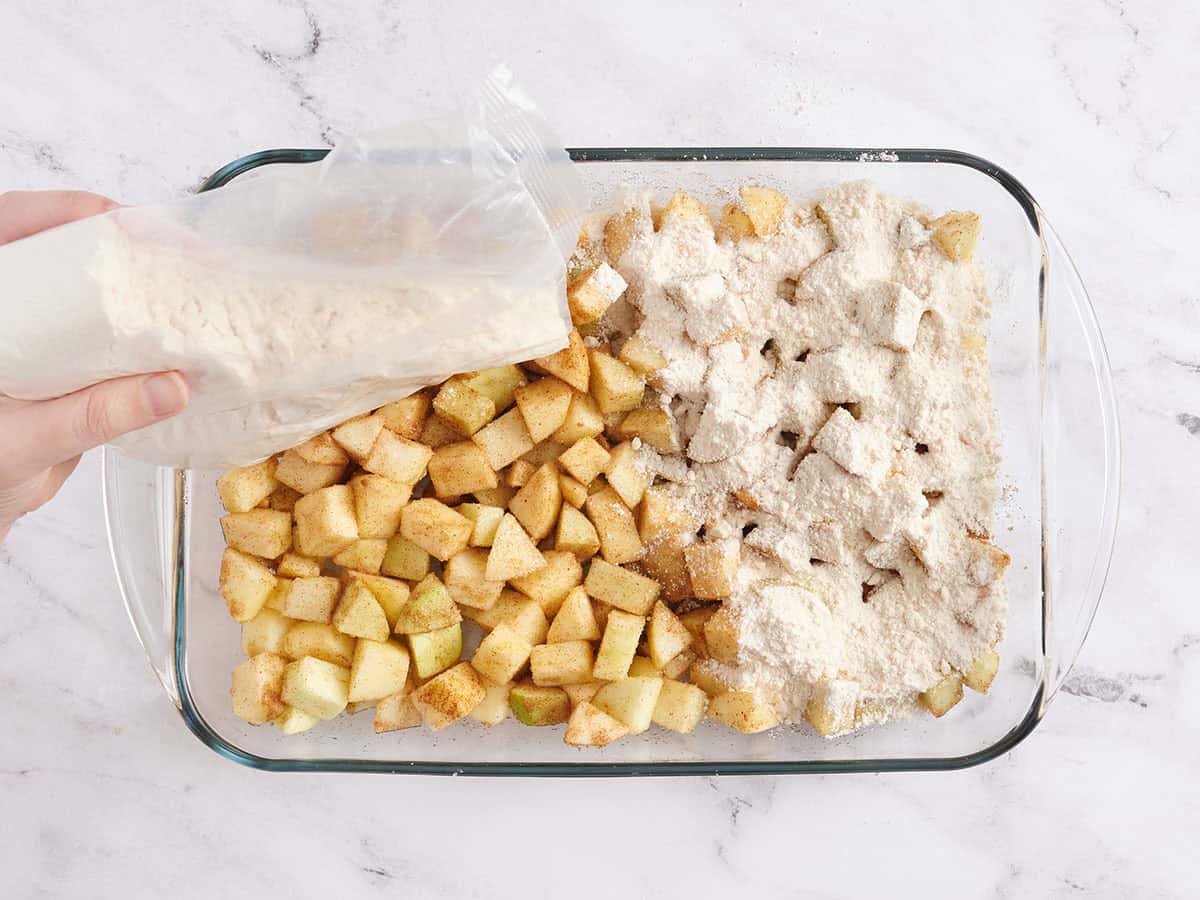 Cake mix being sprinkled over seasoned apples in a baking dish.