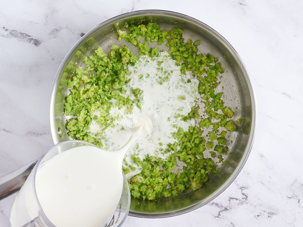 Cream being poured into a sauce pan with diced broccoli.
