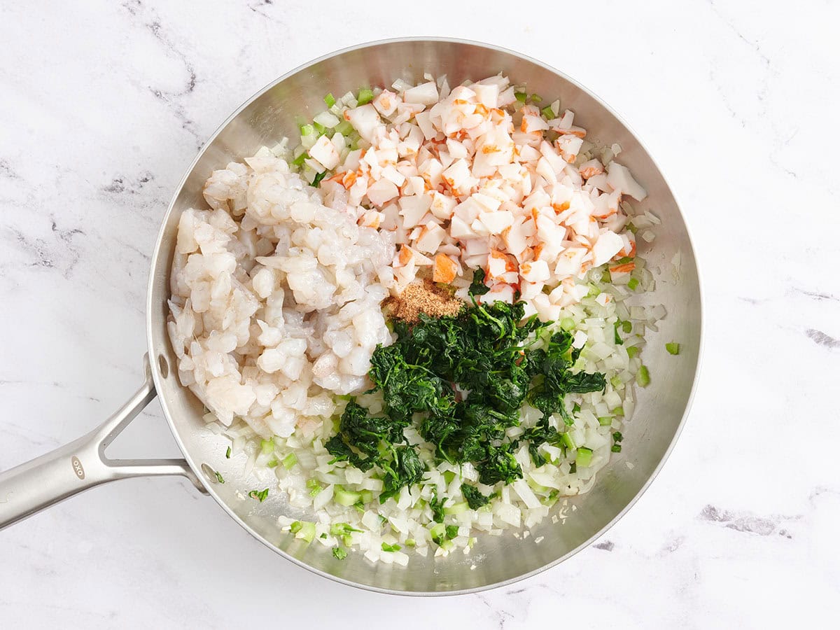 Shrimp, imitation crab, spinach and mire poix in a skillet.