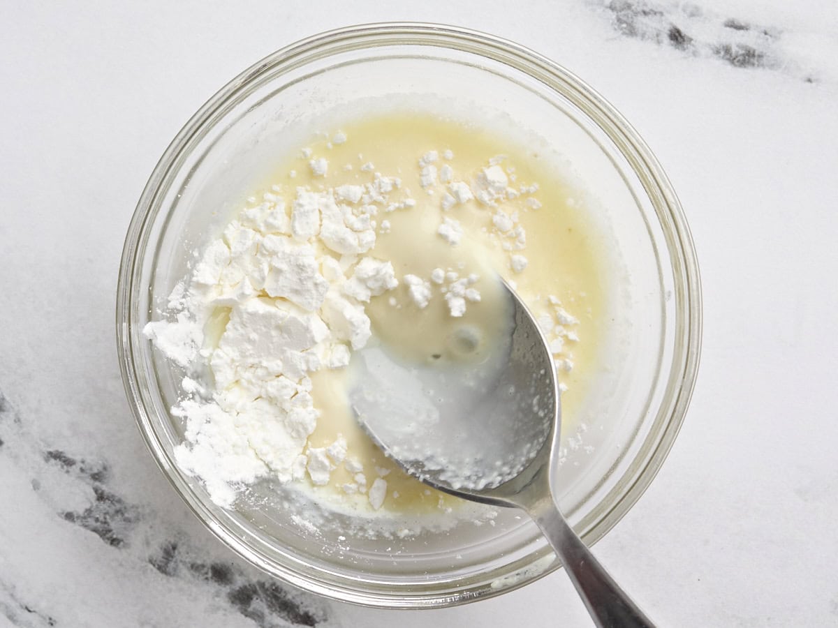 Milk and cornstarch in a bowl being mixed with a spoon.