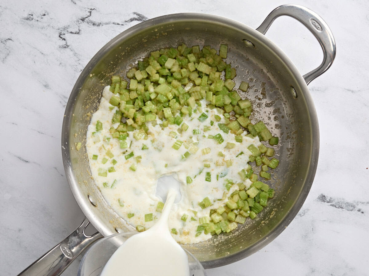 Cream being poured into a saucepan of diced celery.