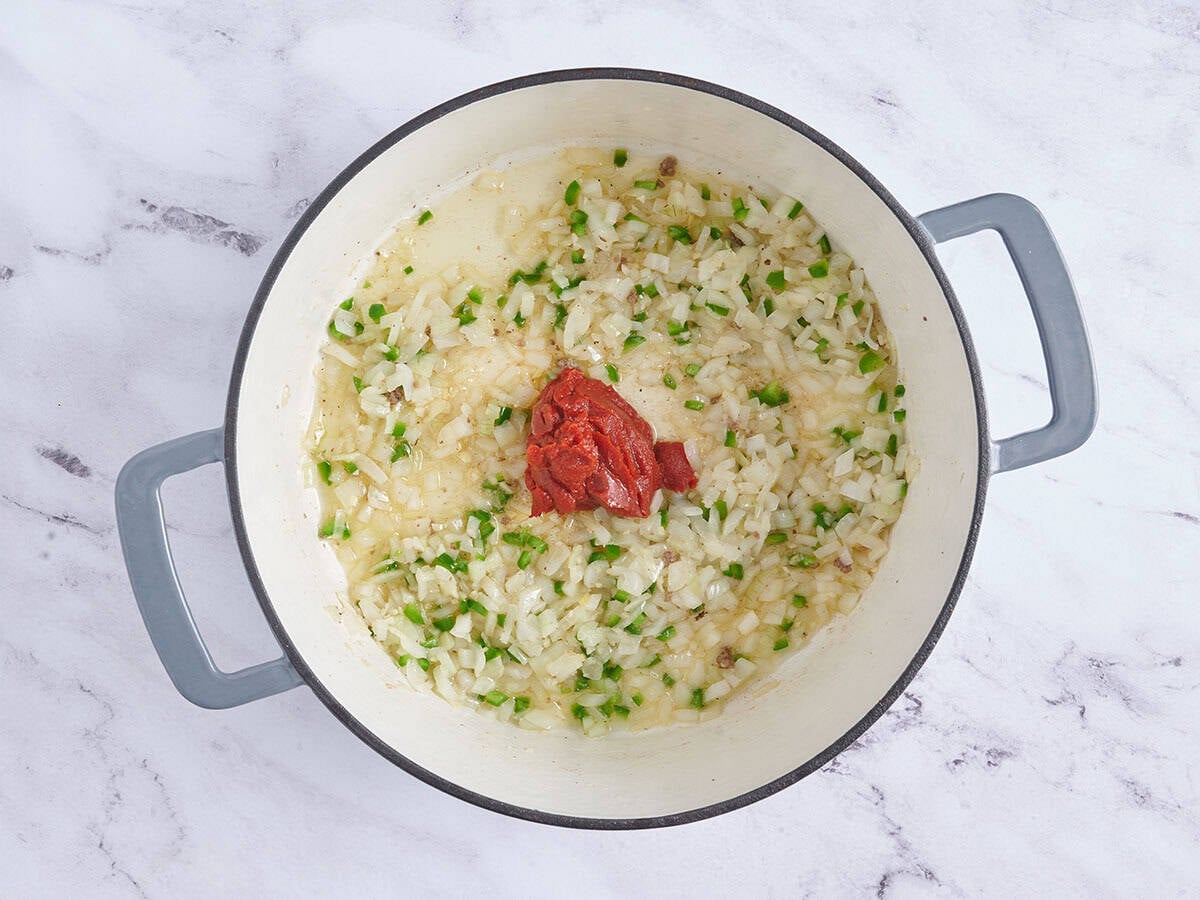 Tomato paste added to sauteed onions and jalapenos in a pot.