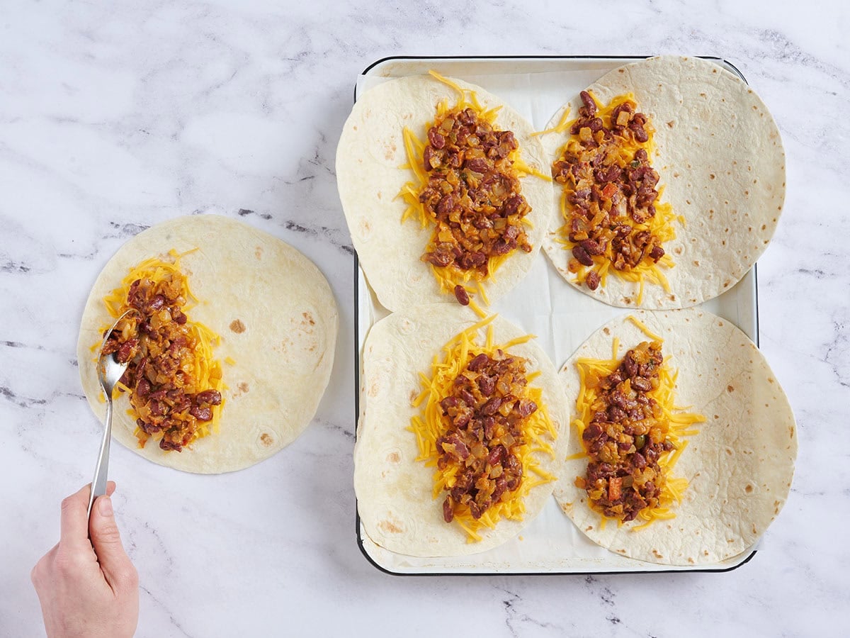 Flour tortillas topped with shredded cheddar cheese and beans.