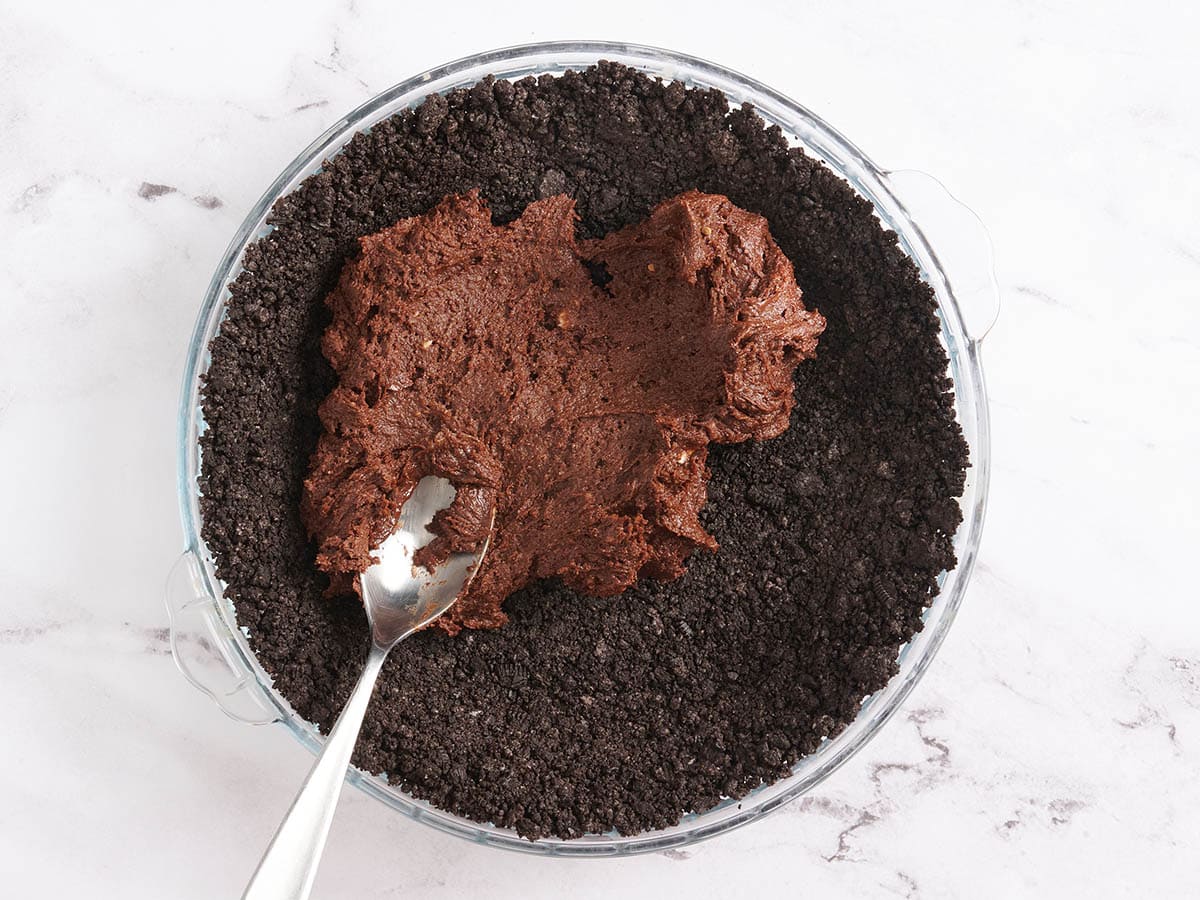 Brownie batter being spread on a chocolate pie crust.