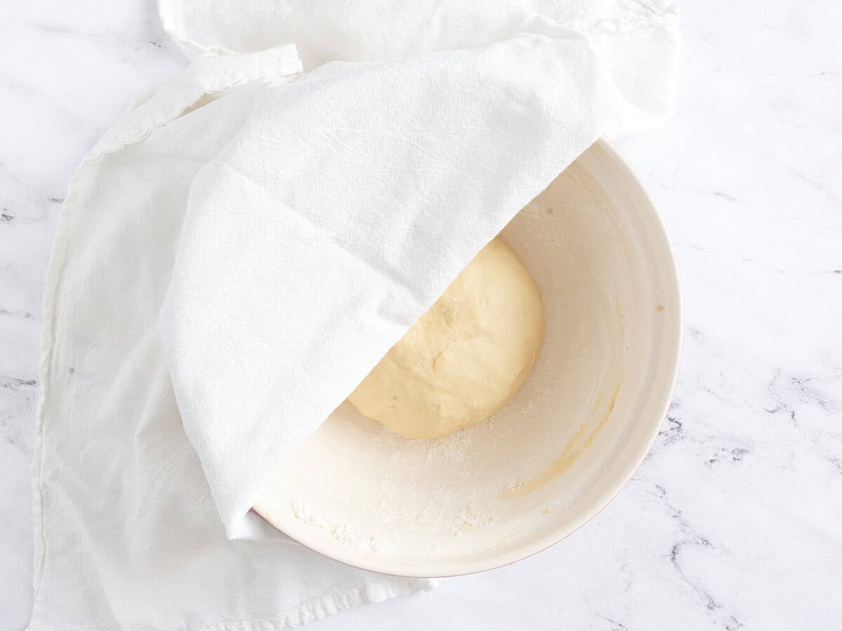Dough ball in a bowl partially covered for proofing.