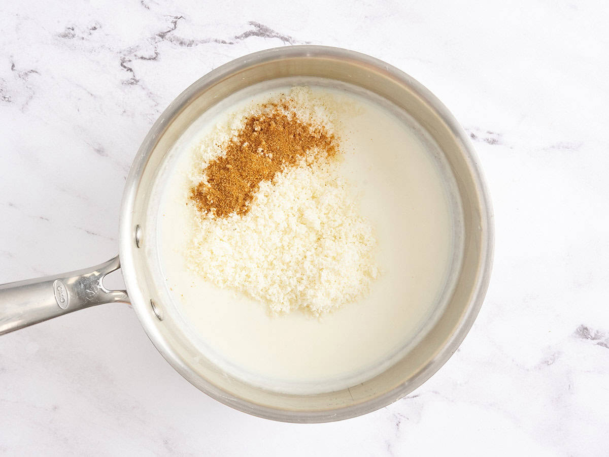 Parmesan and seasonings in a white cream sauce in a saucepan.