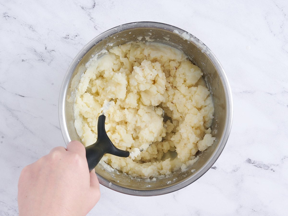 A hand using a masher to mash cooked potatoes in an instant pot.