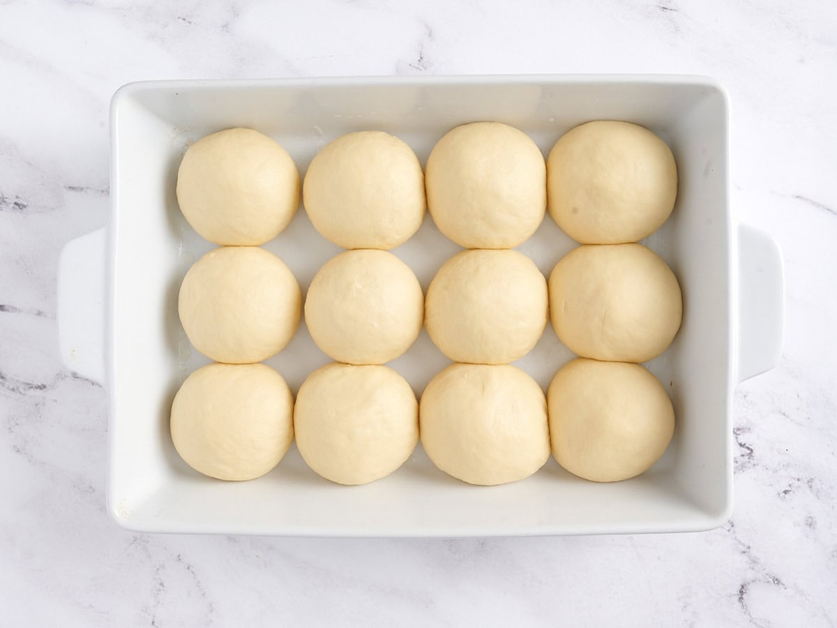 Proofed rolls in a white baking dish.