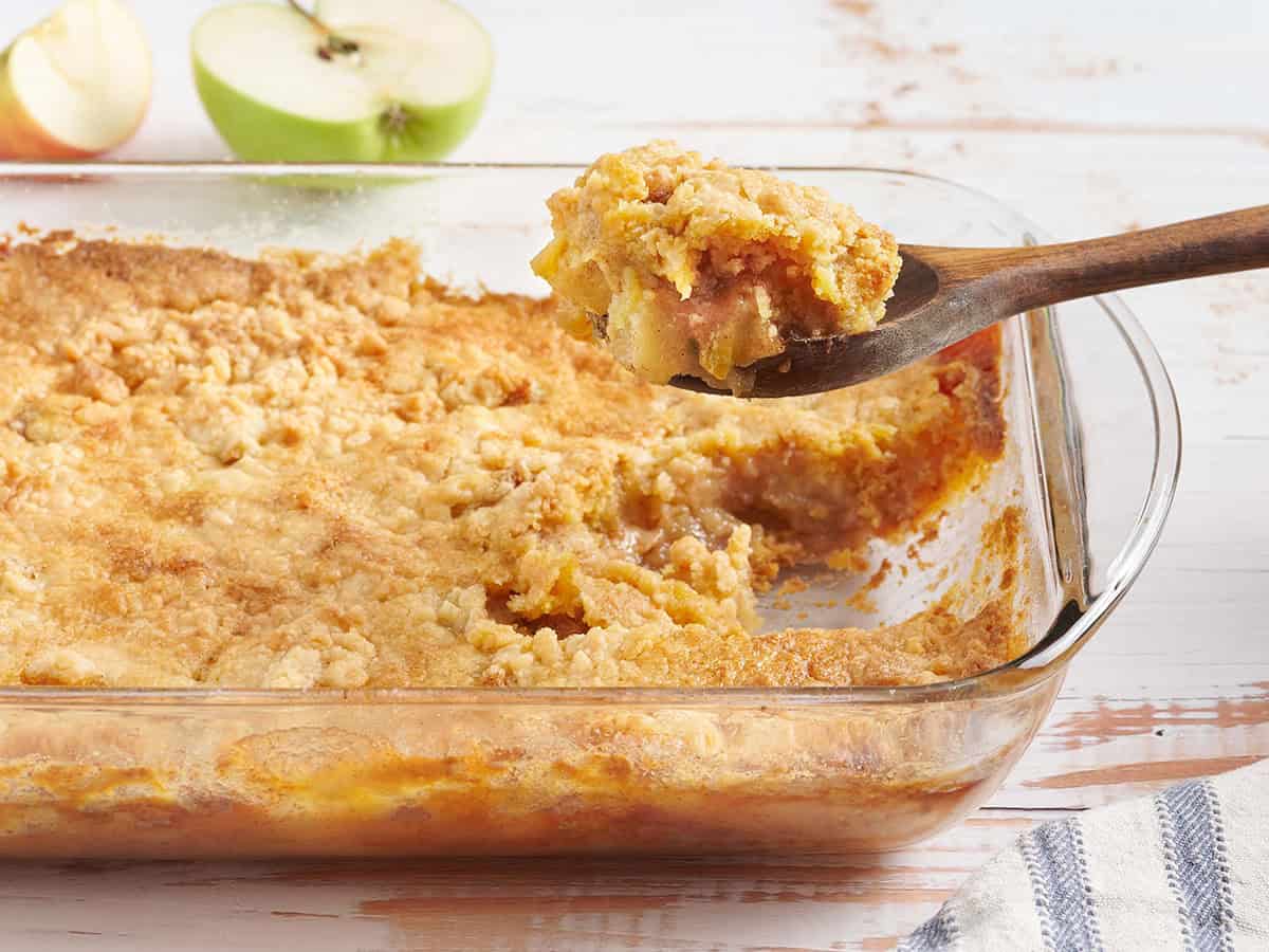 Side view of an easy apple dump cake in a baking dish with a serving spoon taking some.
