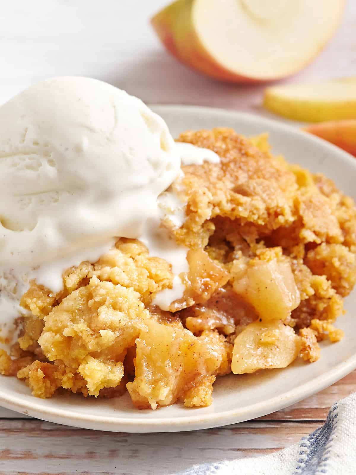 Side view of apple dump cake on a plate with a scoop of vanilla ice cream.