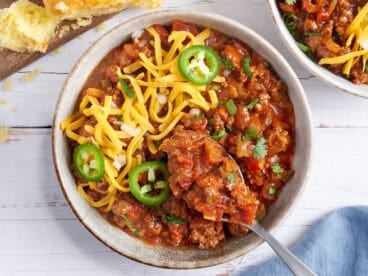 Overhead view of a bowl of Texas chili topped with shredded cheese and jalapeno slices with a spoon taking some.