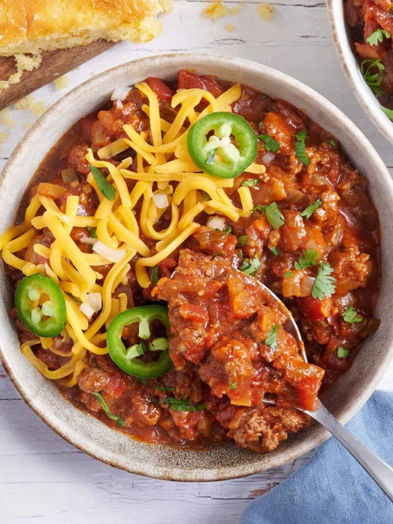 Overhead view of a bowl of Texas chili topped with shredded cheese and jalapeno slices with a spoon taking some.