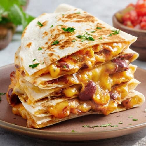 Side view of a stack of cheesy kidney bean quesadillas on a plate.