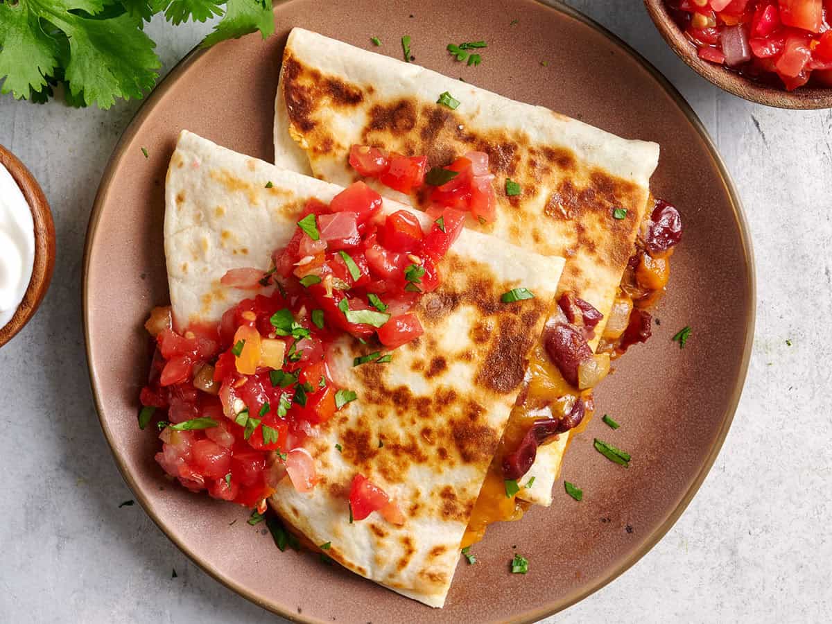 Overhead view of two kidney bean quesadillas on a plate with salsa.