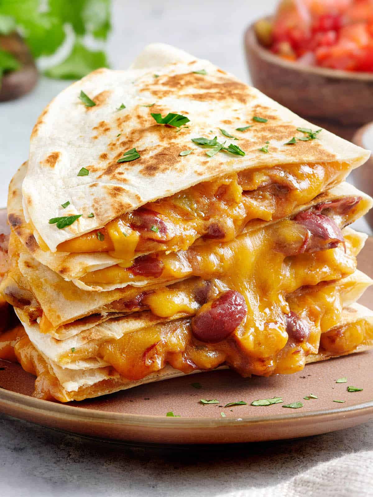 Side view of a stack of cheesy kidney bean quesadillas on a plate.