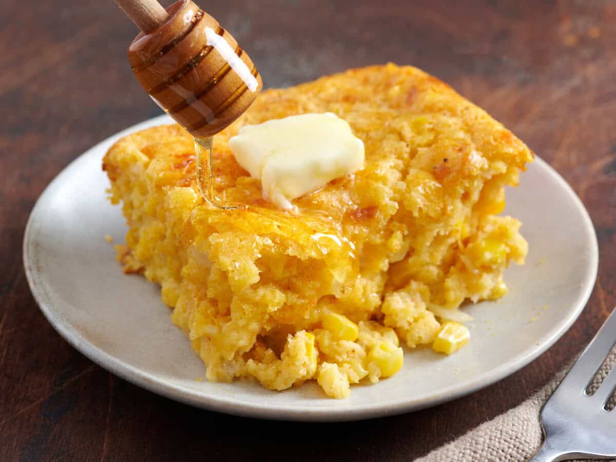 Cornbread casserole on a plate with a pat of melting butter and honey being drizzled on top.