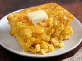 Cornbread casserole on a white plate with a pat of melting butter.
