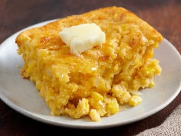 Cornbread casserole on a white plate with a pat of melting butter.