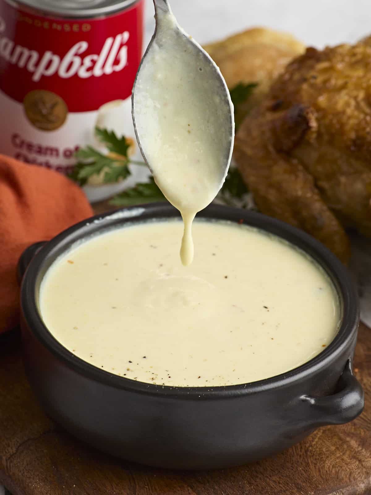 Side view of cream of chicken soup in a bowl with a spoon dripping soup back into the bowl.