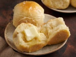 Hawaiian rolls on a plate. one with a pat of melting butter.
