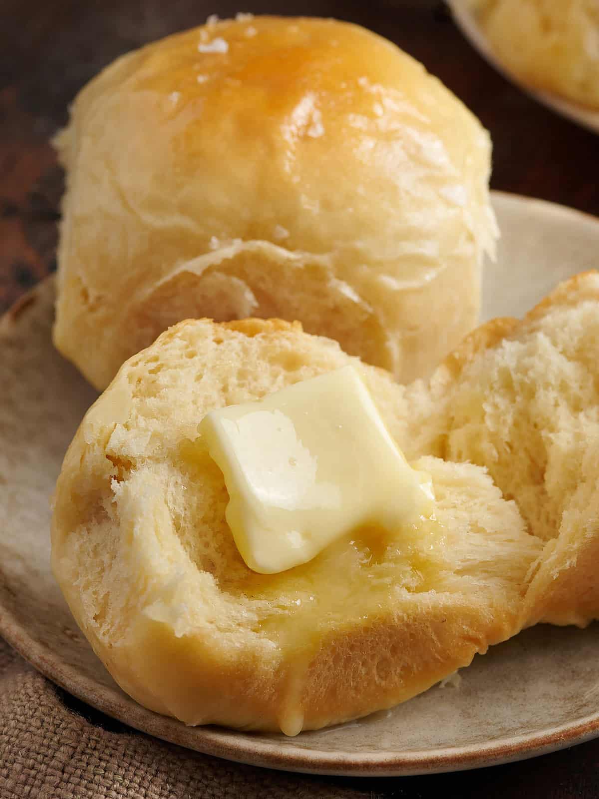 Two Hawaiian rolls on a plate, one cut open with a pat of melting butter on it.