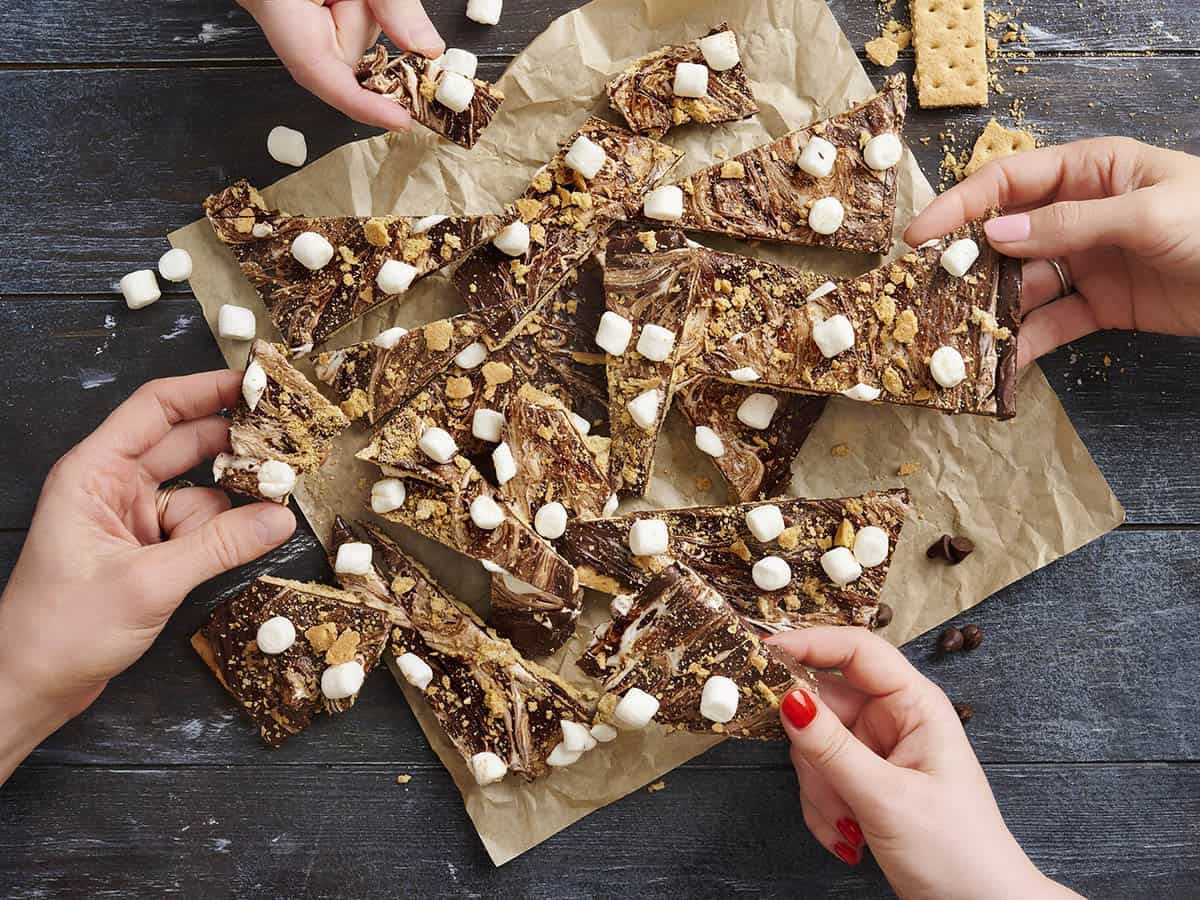 overhead image of s'mores bark and various hands taking pieces