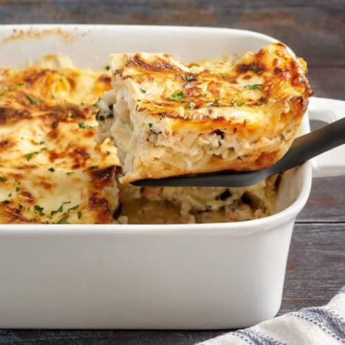 Side view of a homemade seafood lasagna, with a slice being removed from the baking dish.