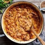 Overhead view of shredded pork and sauerkraut in a pot with a wooden spoon.