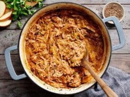 Overhead view of shredded pork and sauerkraut in a pot with a wooden spoon.