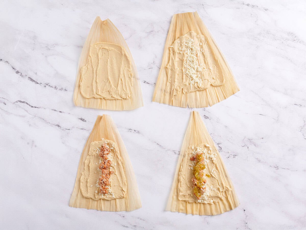 Corn husks being filled with tamale mixture.