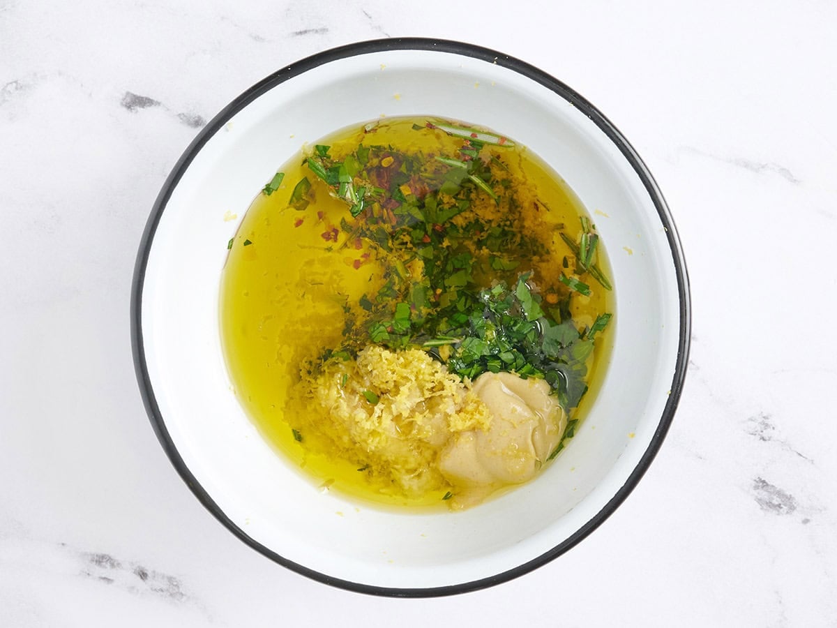 Olive oil, mustard and herbs in a bowl.