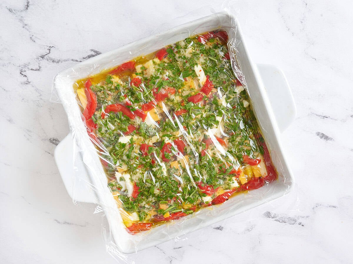 A baking dish of marinaded cheese covered with plastic wrap.