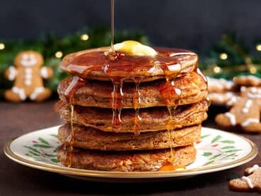 Side view of a stack of gingerbread pancakes with butter and syrup being drizzled over.