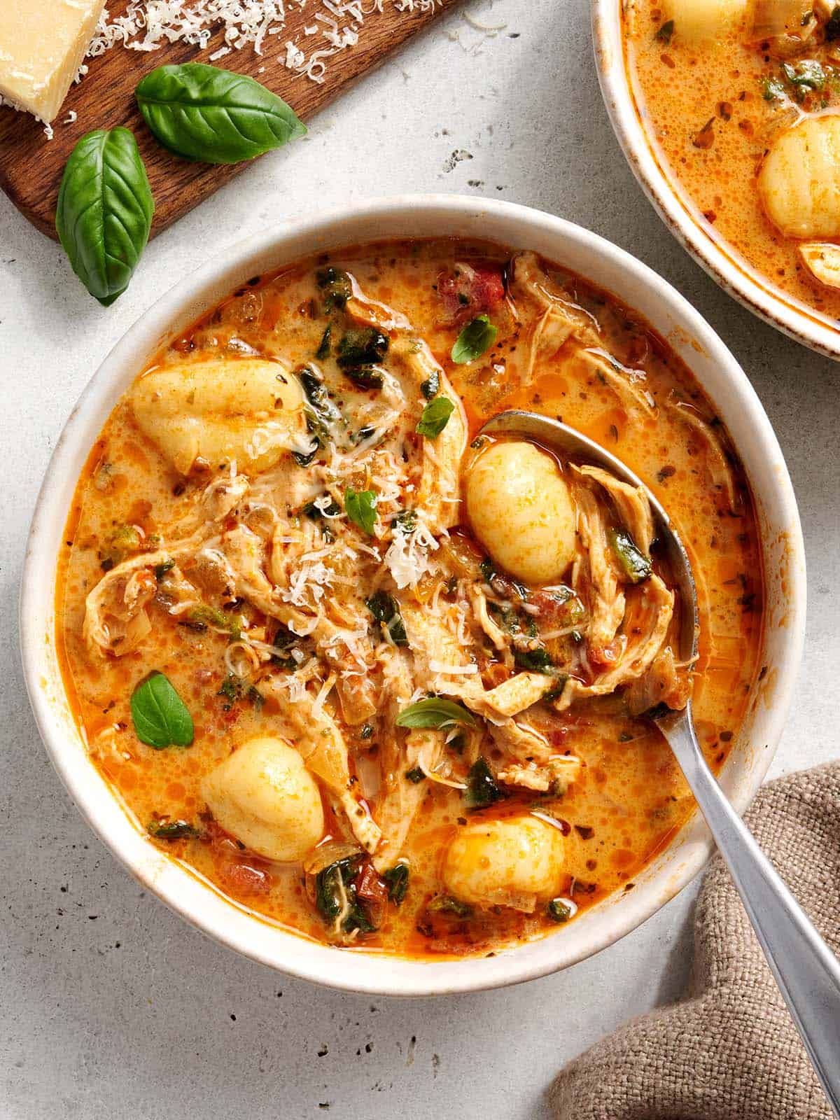 White bowl of marry me chicken soup with a spoon in it. 