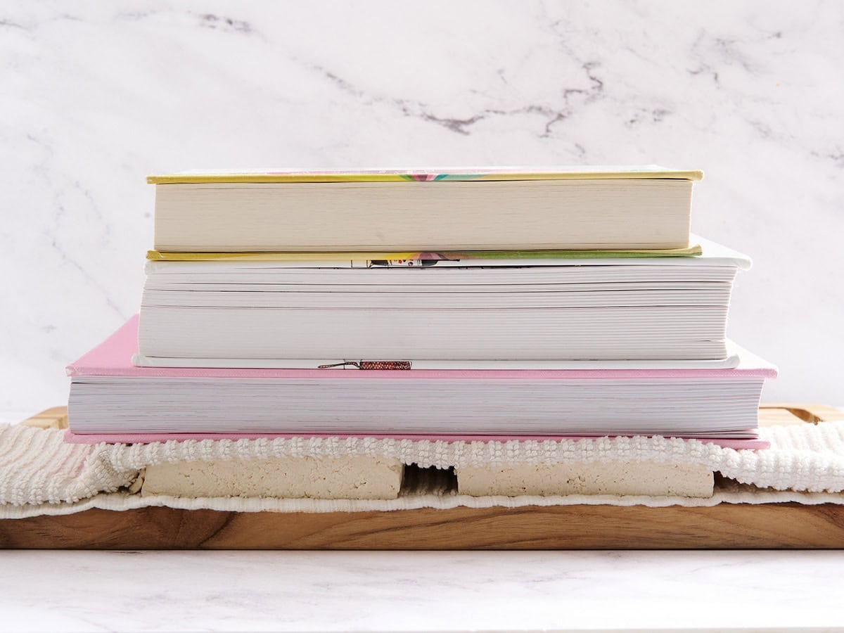 Books stacked on top of tofu on a wooden cutting board.