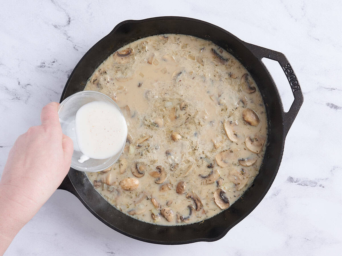 Cornstarch slurry being poured into a skillet of chicken filling.