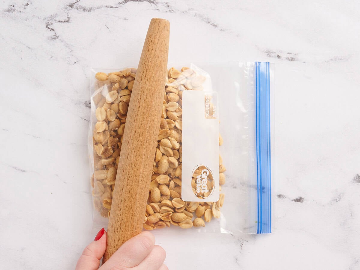 Peanuts in a bag being crushed by a rolling pin.