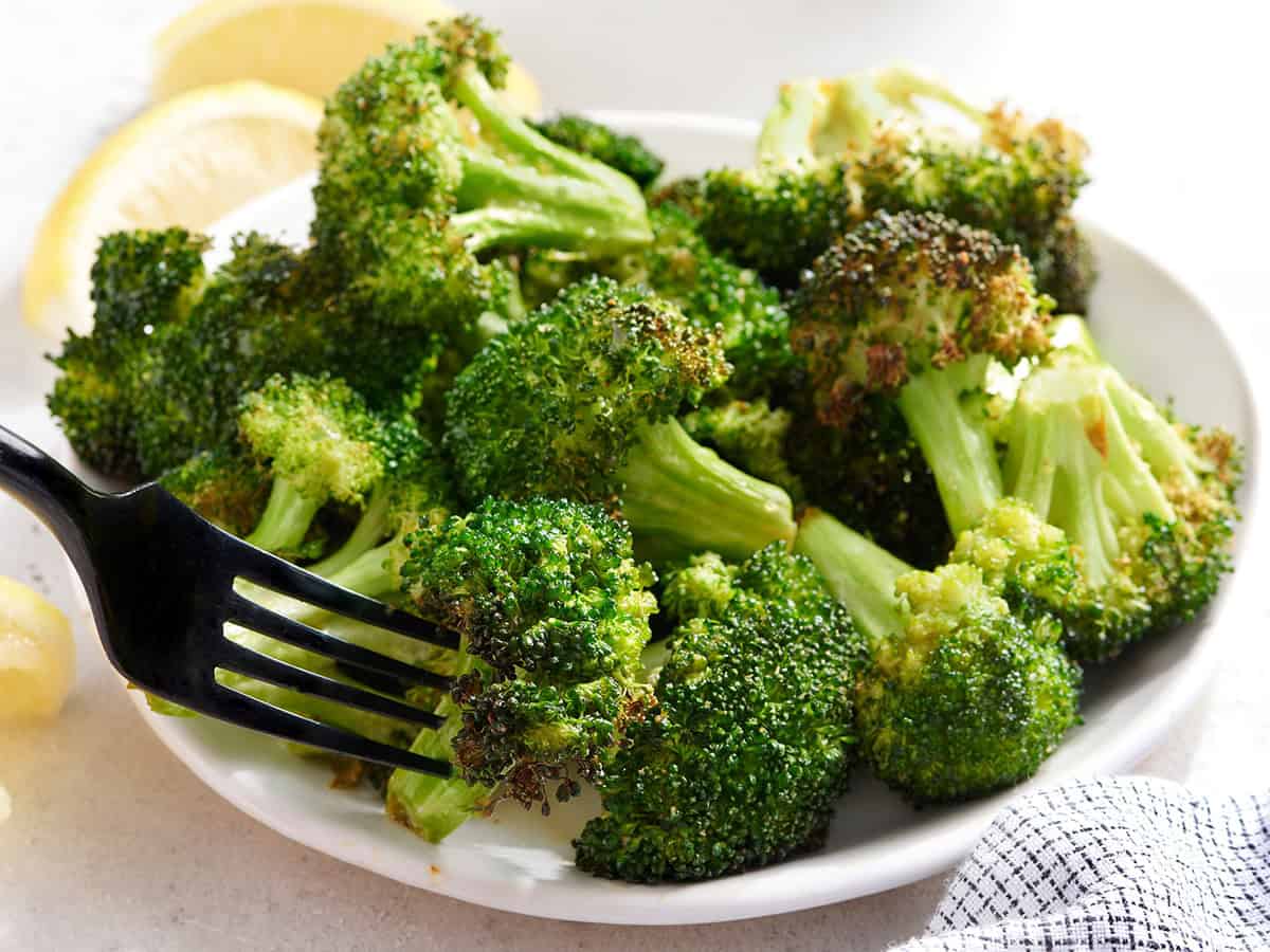 Side view of air fryer broccoli on a plate with a fork taking one.