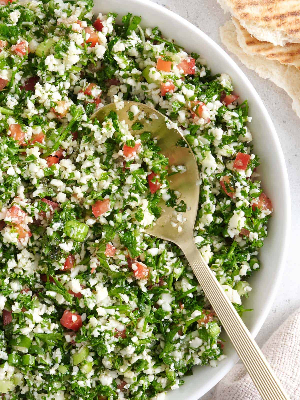 Overhead close up view of a bowl of cauliflower tabbouleh with a spoon.