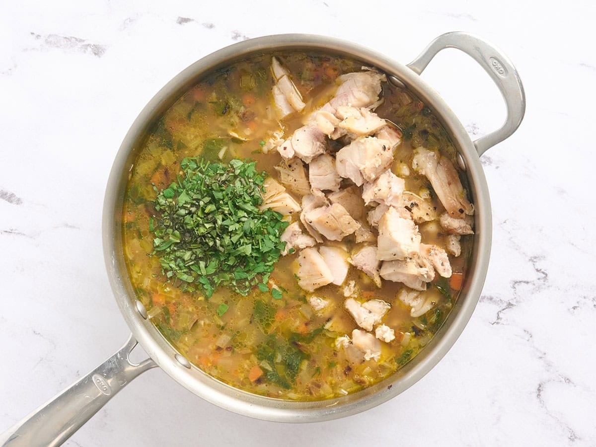 Fresh herbs and diced chicken added to a pot of brothy rice.