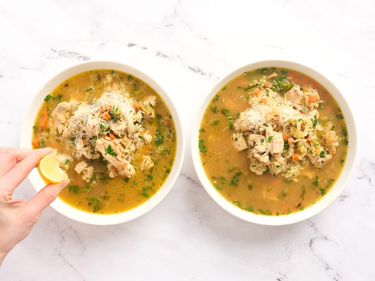 Two bowls of brothy rice with a hand squeezing lemon over one.